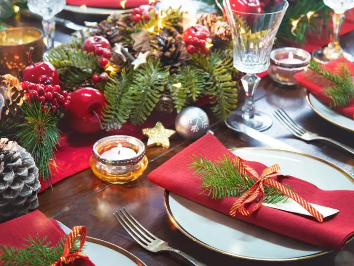 Vackert dukat julbord med röda servetter, granris, äpplen, kottar och ljus. Här ser du vad man har på ett julbord för att skapa julstämning.