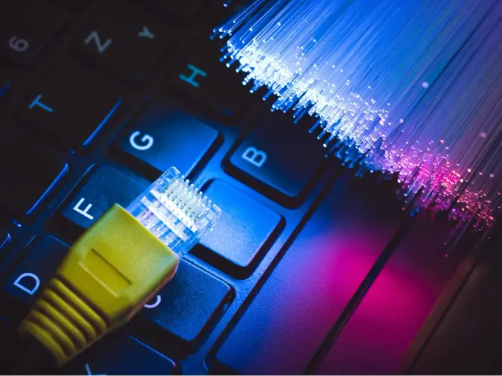 Connessione internet: un cavo giallo su tastiera e fibre ottiche luminose. Capire cos'è l'ADSL è fondamentale per la tua navigazione.