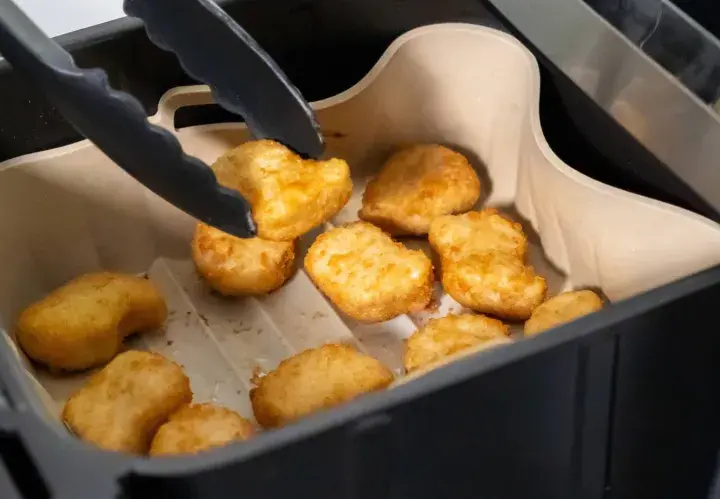 Tång tar upp gyllene, krispiga tater tots ur en airfryer.
