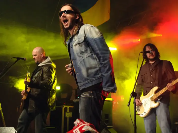 Energetyczne kapele punkowe z lat 80. na scenie, w dymie i kolorowych światłach. Wokalista krzyczy do mikrofonu, gitarzysta gra na basie.