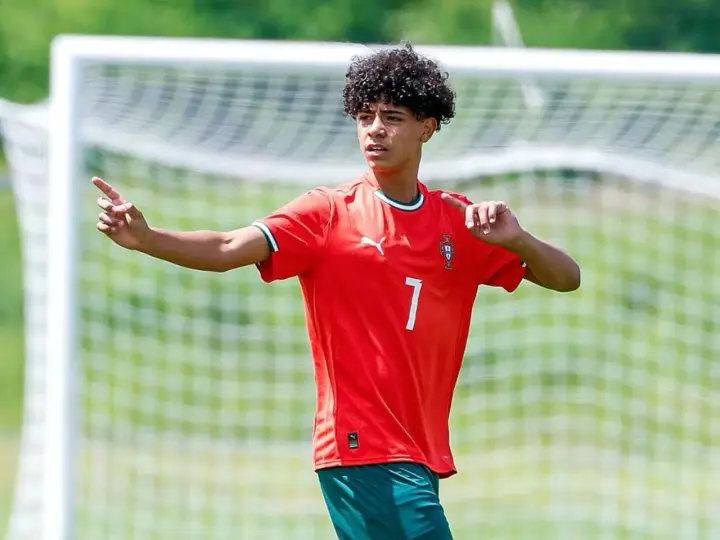 Cristiano Ronaldo Jr. con pelo rizado y camiseta roja con el número 7, señalando con el dedo índice.