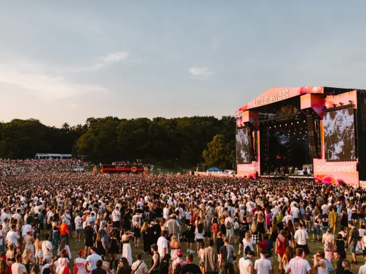 Tłum ludzi na festiwalu Bittersweet 2026, podziwiający scenę z wielkim ekranem i artystami. Słońce zachodzi, tworząc ciepłą atmosferę.