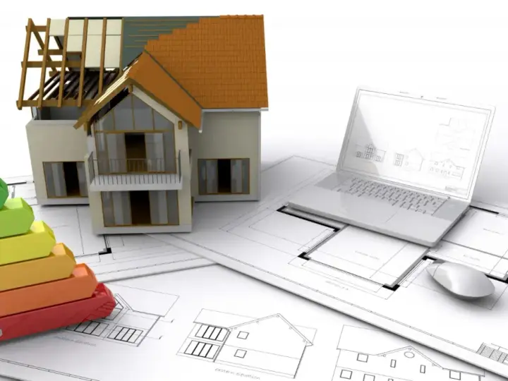 Maquette de maison, échelle d'énergie, plans et ordinateur portable. L'isolation RGE Qualibat est essentielle pour une maison performante.