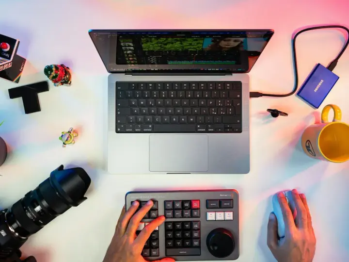 Un escritorio con un portátil mostrando un editor de video, un teclado de control, cámara, disco duro y taza. Ideal para los mejores editores de video para PC.