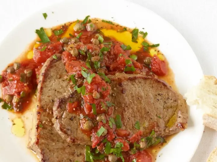 Zwei saftige Scheiben Rindfleisch, bedeckt mit einer würzigen Tomaten-Kapern-Sauce, serviert mit Brot. Ein authentisches Gericht im Stil Pizzaiola original italienisch.