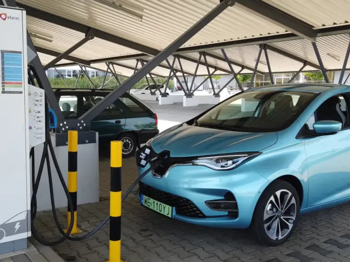 Błękitny Renault Zoe podłączony do ładowarki na parkingu pod zadaszeniem.