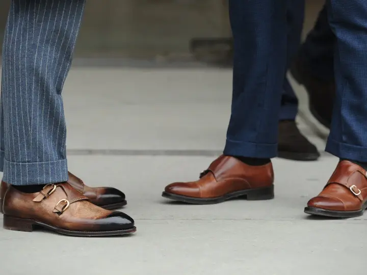 Primo piano su scarpe monk strap marroni e diversi tipi di orlo pantaloni: a risvolto e con pinces.