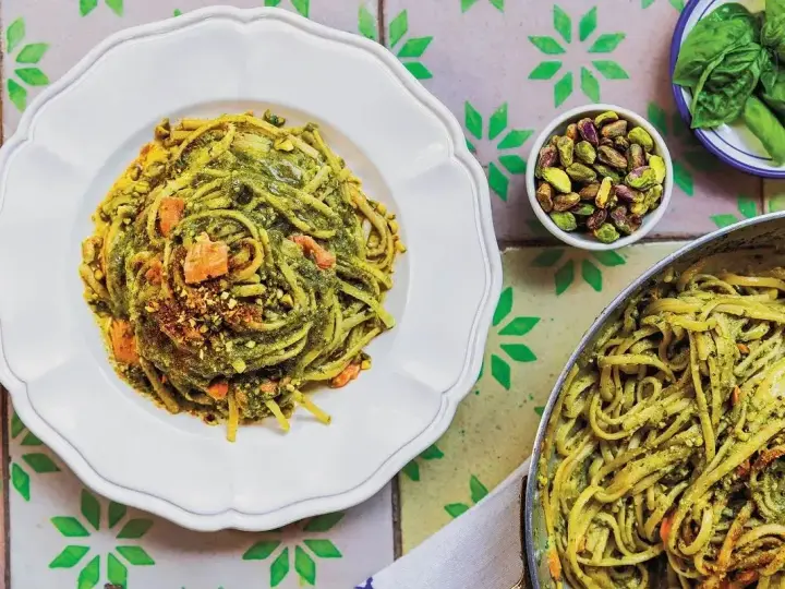Pyszny makaron z zielonym pesto i pistacjami, wyglądający jak makaron jak z restauracji. Obok miseczka z pistacjami i listki bazylii.