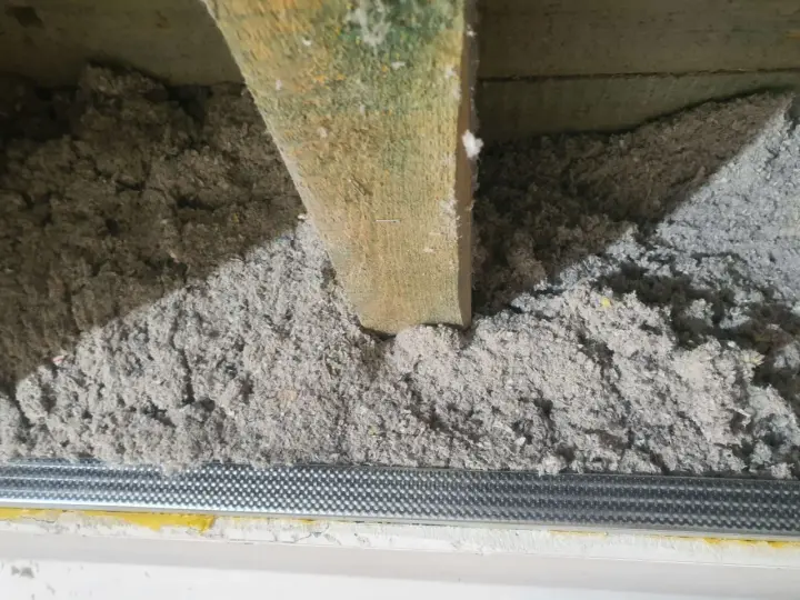 Izolacja z celulozy wypełnia przestrzeń między drewnianymi belkami stropowymi, tworząc warstwę termoizolacyjną.