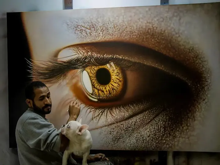 Un artiste achève une peinture hyperréaliste d'un œil doré, son bouledogue français curieux observant le processus créatif.