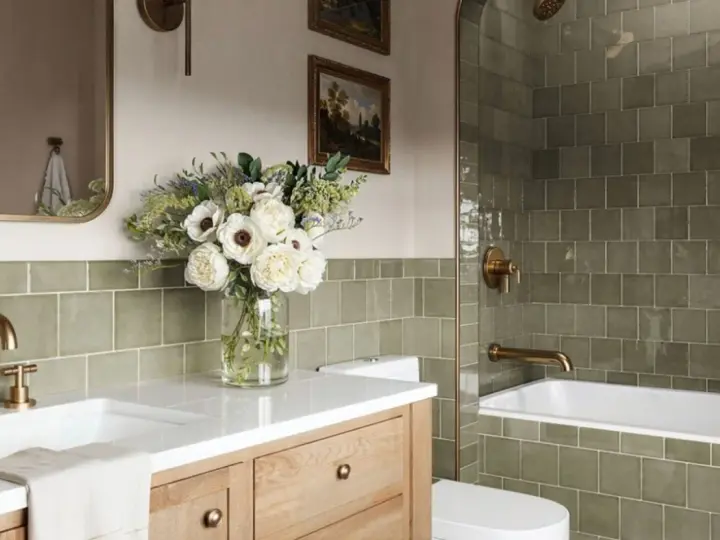 Élégante salle de bain verte avec carrelage texturé, vasque en bois, bouquet de fleurs blanches et robinetterie dorée.