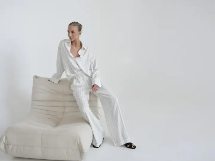 Elegancka kobieta w pasiastym komplecie, uosobienie quiet luxury, siedzi na kremowej sofie.