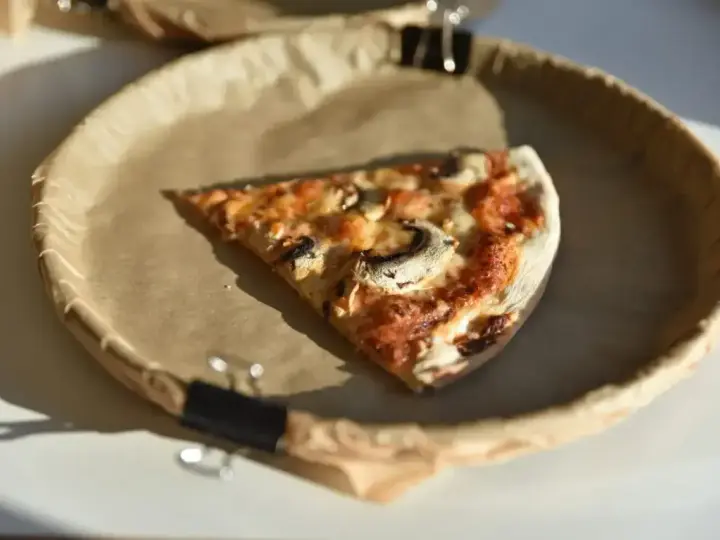 Kawałek pizzy z pieczarkami na brązowym papierze. Zastanawiasz się, ile kalorii ma pizza?