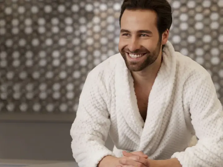Uomo sorridente in un morbido accappatoio che asciuga bene, con uno sfondo a mosaico.