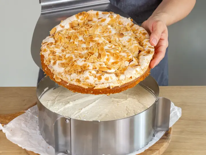 Eine köstliche Stachelbeer Baiser Torte mit Mandel-Topping wird gerade in einen Tortenring gesetzt.