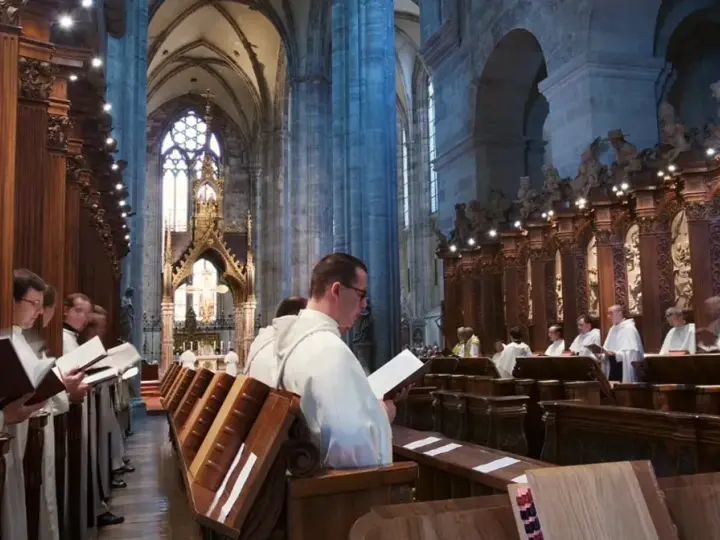Men in white robes read from books in a grand cathedral, likely participating in matins, a morning prayer service.