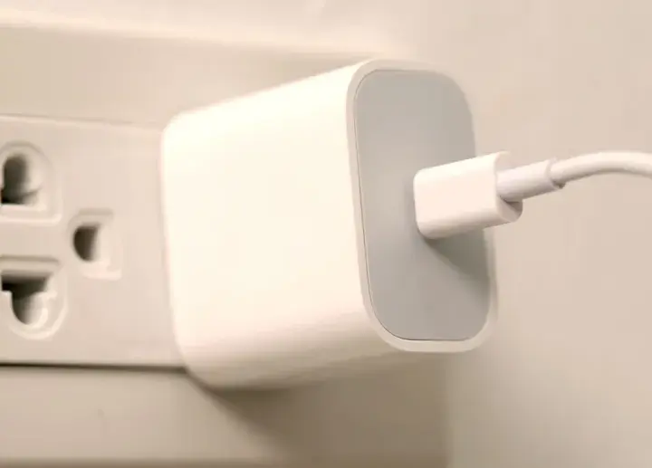 Biała ładowarka z kablem podłączona do gniazdka elektrycznego. Typ wtyczki EU.