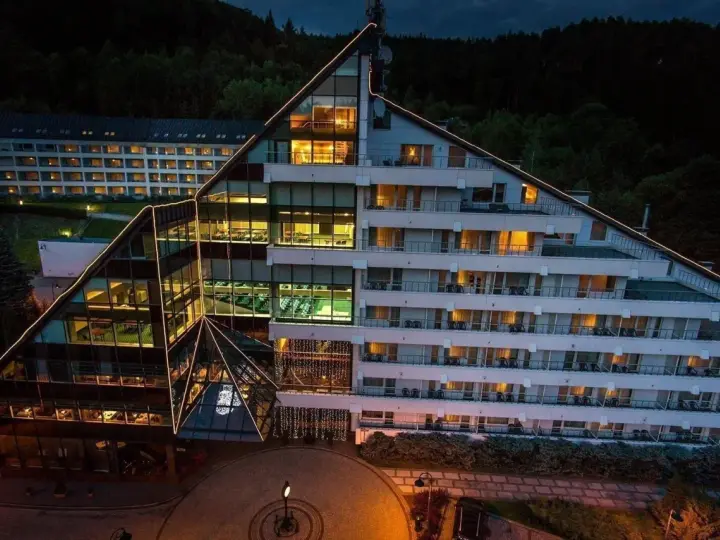 Nowoczesny hotel Klimczok Resort & Spa nocą, z oświetlonymi oknami i wejściem. Wiele pozytywnych hotel klimczok resort & spa opinie potwierdza jego urok.