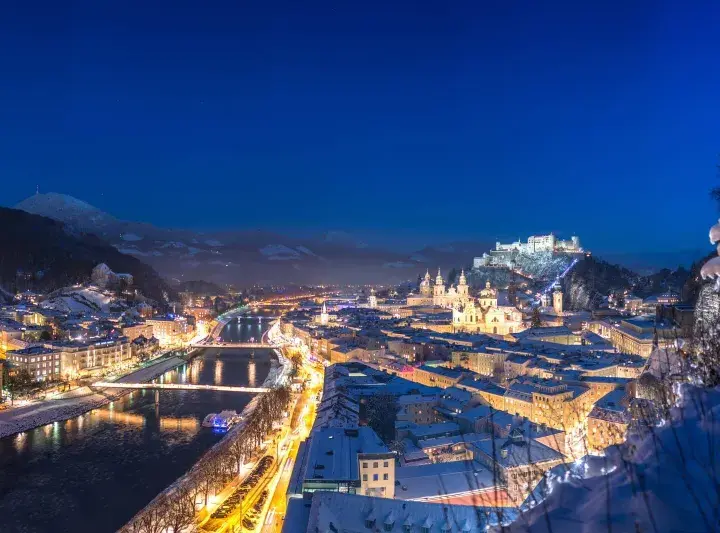Magiczne salzburg zimą. Oświetlone miasto, rzeka Salzach i górująca twierdza Hohensalzburg w śnieżnej scenerii nocą.
