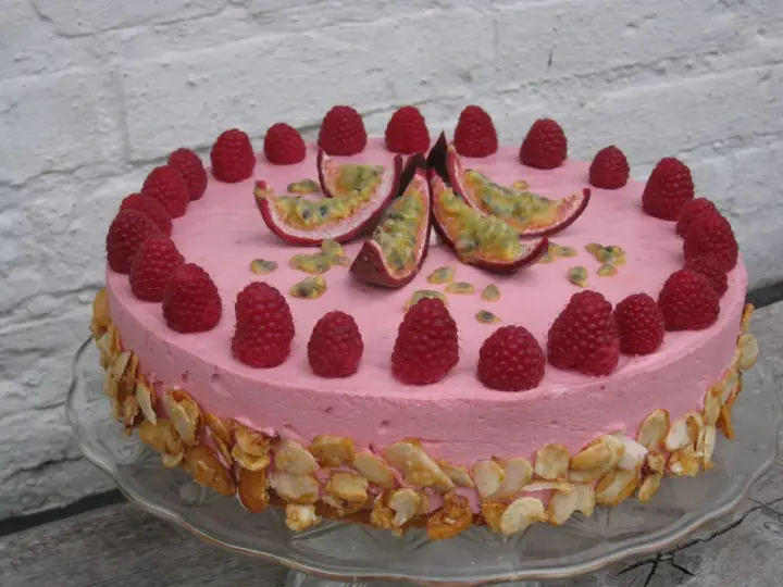 En rosa hallonmousse tårta dekorerad med färska hallon och passionsfrukt. Kanterna är täckta med rostade mandelflagor.
