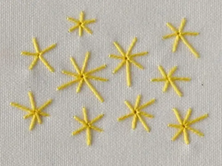 Piccole stelle gialle ricamate a punto pieno su tessuto bianco. Un esempio di come ricamare una stella a punto pieno.