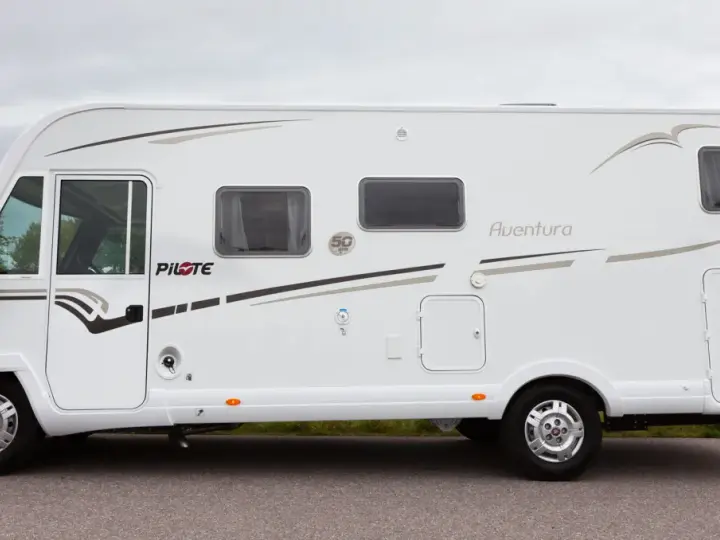 Vit husbil, Pilote G740 Aventura, parkerad vid en väg med gräs och träd i bakgrunden.
