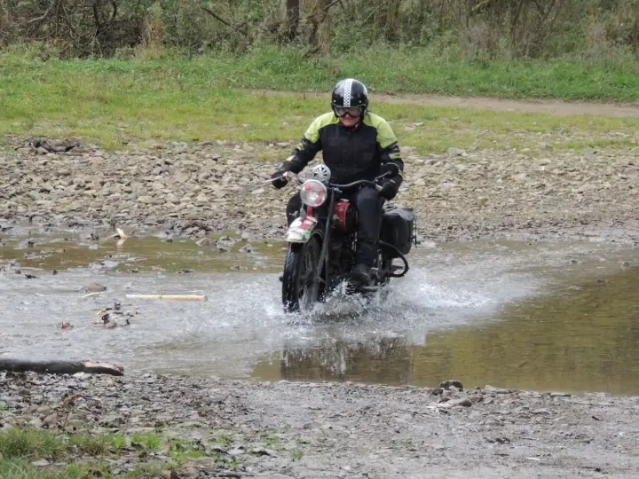 Motocyklista w kasku pokonuje wodną przeszkodę na kamienistej trasie w okolicach Jasła.