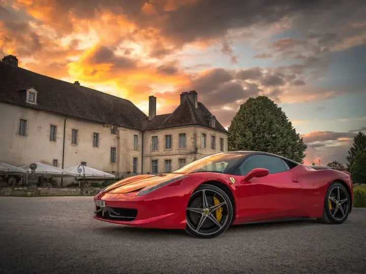 Czerwone Ferrari zaparkowane przed zabytkowym budynkiem podczas zachodu słońca.