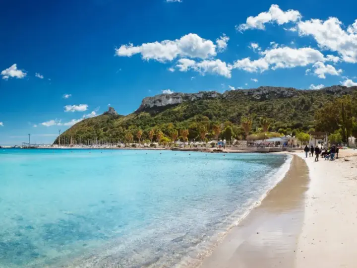 Spiaggia con acque cristalline e la sagoma della Sella del Diavolo all'orizzonte, sotto un cielo azzurro con nuvole bianche.