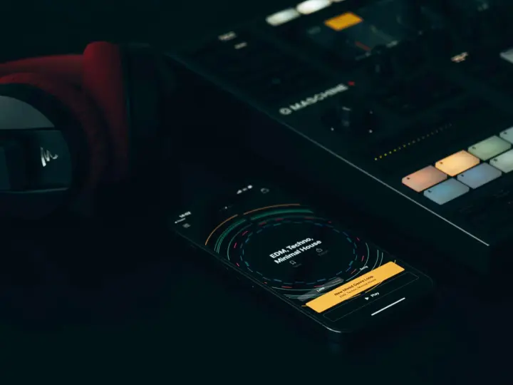 Czerwone słuchawki, kontroler Maschine i smartfon z aplikacją do tworzenia muzyki, gdzie widać koala sampler.