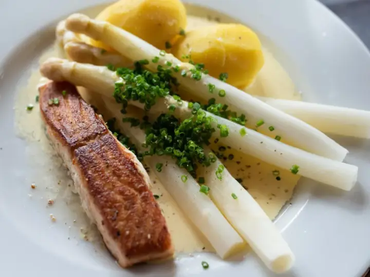 Ein Stück Lachs mit Spargel, Kartoffeln und Sauce Hollandaise. Der Spargel ist mit Schnittlauch bestreut.