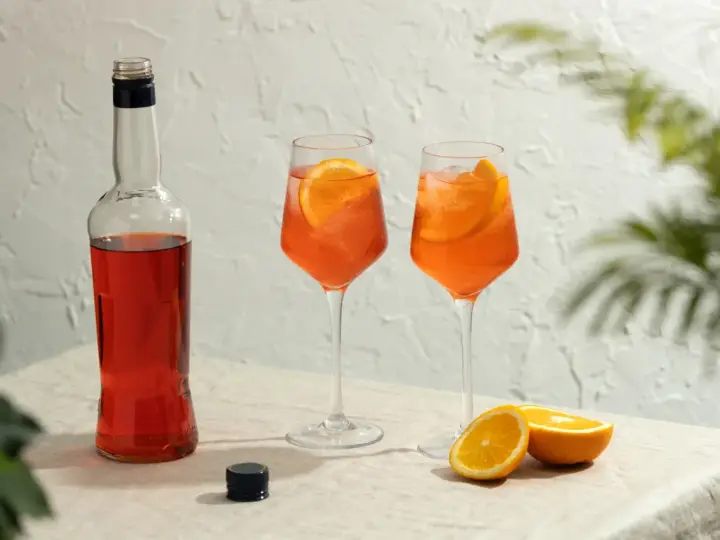 Dwa orzeźwiające drinki aperol z colą, ozdobione plasterkami pomarańczy, stoją obok butelki aperolu.