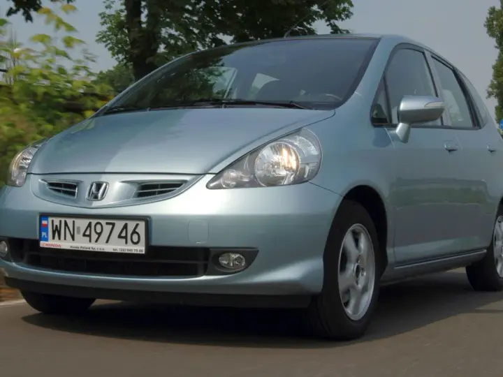 Jasnoniebieski Honda Jazz 2 na drodze, z zielenią w tle.
