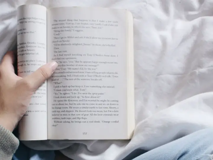 Mano sosteniendo un libro abierto con relatos cortos para mujeres. La página muestra texto y el número 157.