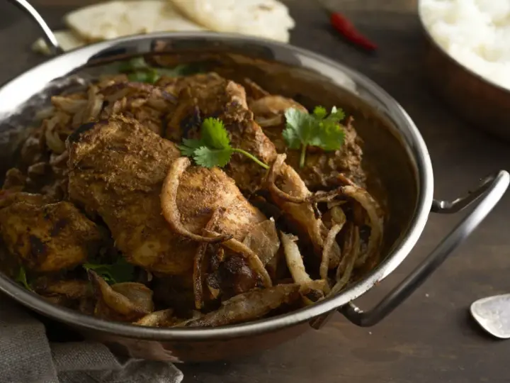 Kurczak w sosie garam masala z cebulą i kolendrą w metalowej misie.