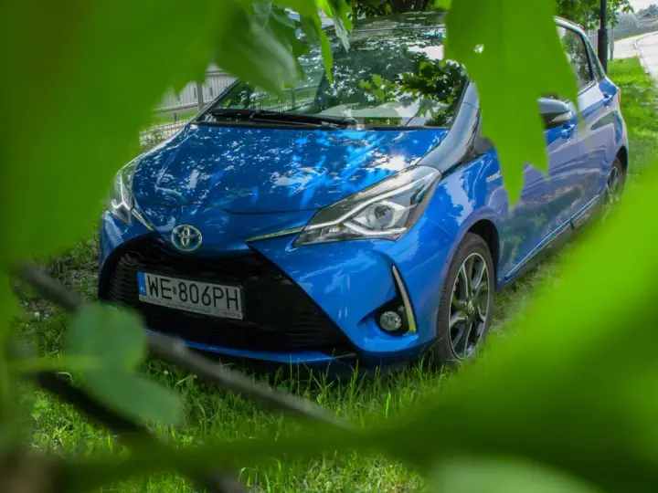 Niebieski Toyota Yaris Hybrid. Czy warto? Zobacz auto z bliska, ukryte wśród zieleni.