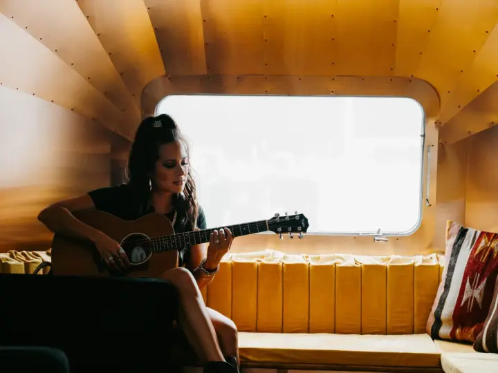 Sarah Jones, piosenkarka, gra na gitarze w przytulnym wnętrzu.