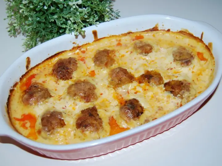 Pulpety w sosie śmietanowo-serowym, zapieczone w naczyniu, z zieloną dekoracją w tle.