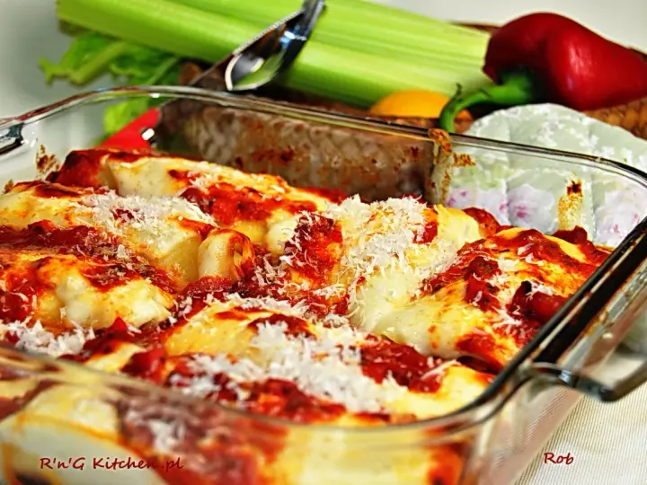 Pyszne, zapiekane cannelloni w sosie pomidorowym, posypane parmezanem. Obok świeże warzywa, idealne do dania.