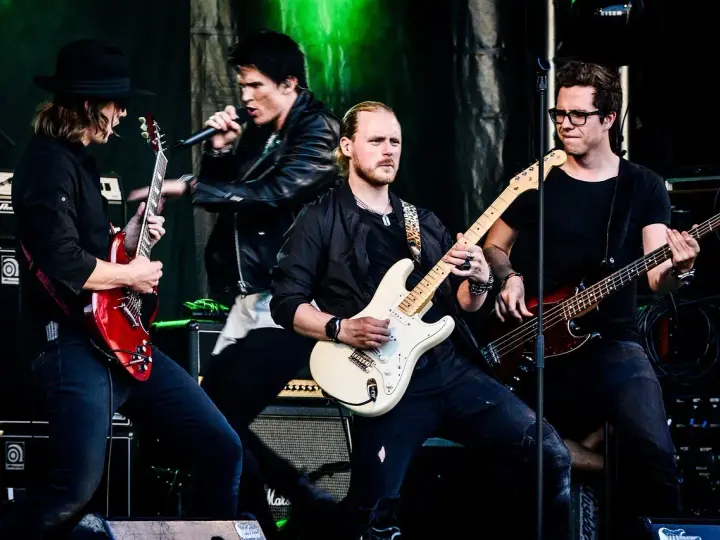 Zespół gra na scenie, wokalista śpiewa, gitarzyści i basista tworzą muzykę. Może to piosenka "Kocham Cię".