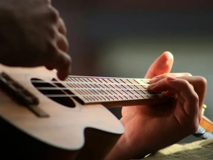 Dłonie grające na ukulele, zbliżenie na gryf i struny.