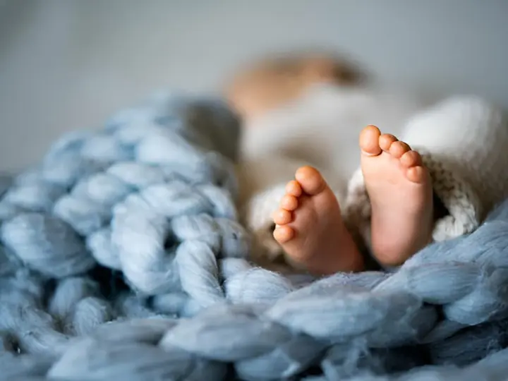 Malutkie stópki dziecka, rozmiar 74 sugeruje wiek około 6-9 miesięcy. Otulone w miękkie kocyki.
