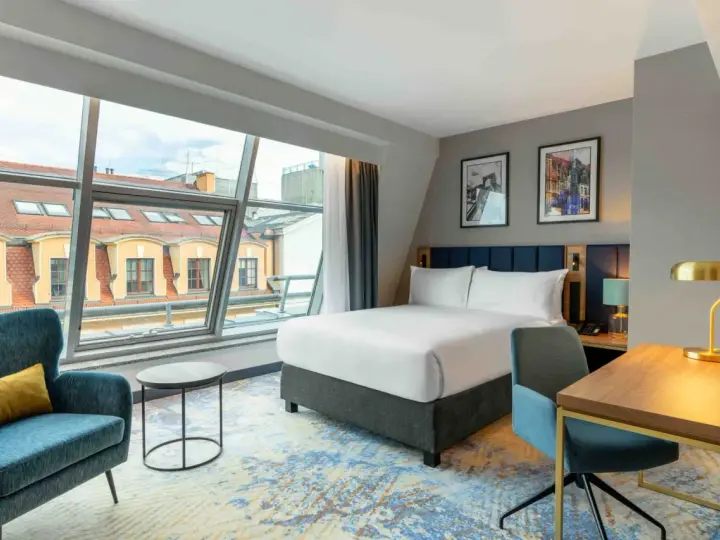 Nowoczesny pokój hotelowy z dużym oknem i widokiem na dachy. Czy zeby zarezerwowac hotel ttzna miec 18 lat? Tak, zazwyczaj.