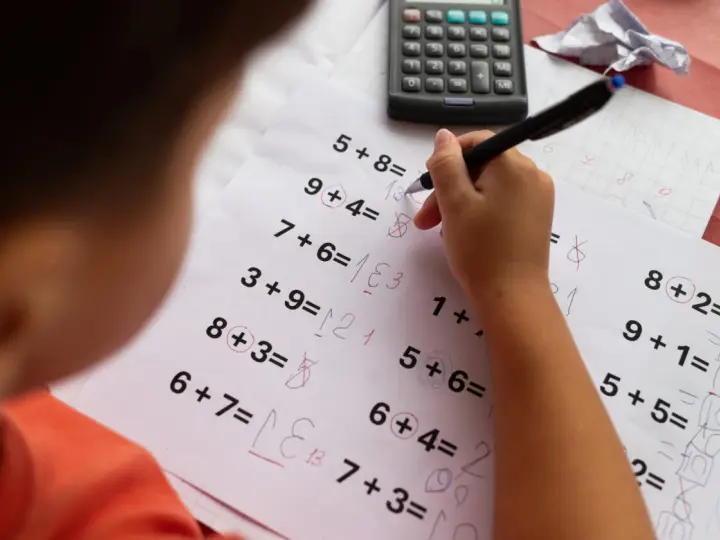 Dziecko rozwiązuje zadania matematyczne, próbując pokonać dyskalkulię. Widoczny kalkulator i zeszyt sugerują naukę.