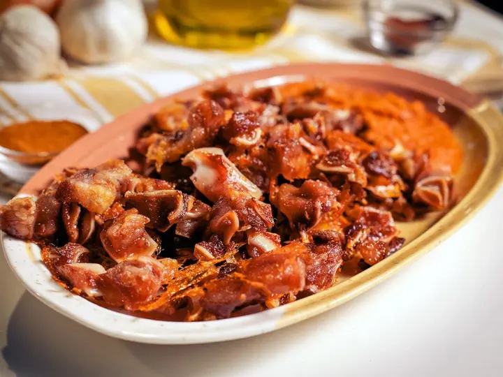 Oreja de cerdo crujiente y dorada servida en un plato con puré naranja.