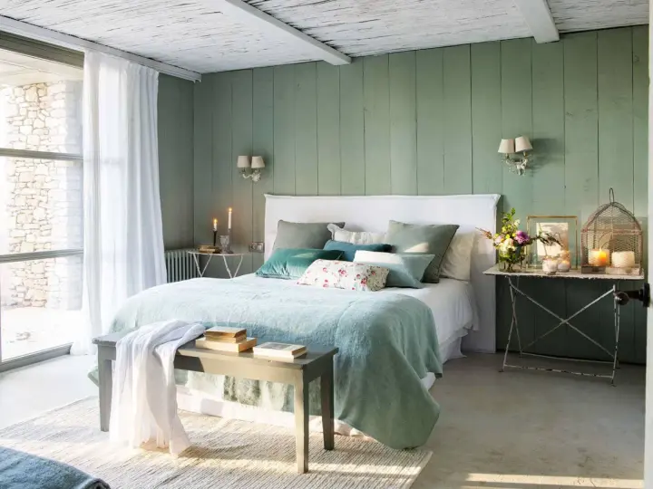 Acogedor dormitorio verde agua y blanco con cama mullida, cojines y luz natural.
