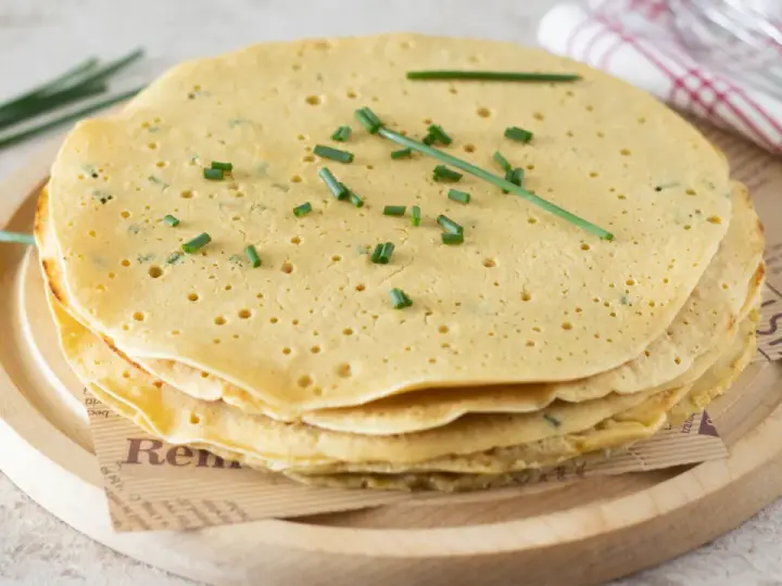 Pila di piadine di ceci dorate, guarnite con erba cipollina fresca. Perfette per un pasto leggero e gustoso.