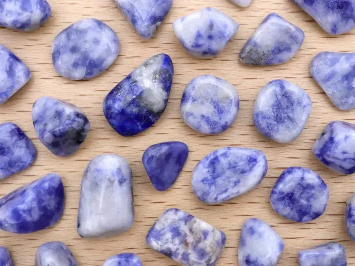 Tumbled sodalite stones, showcasing their deep blue and white patterns. Le pietre di sodalite, con le loro proprietà calmanti, sono disposte su un fondo di legno.