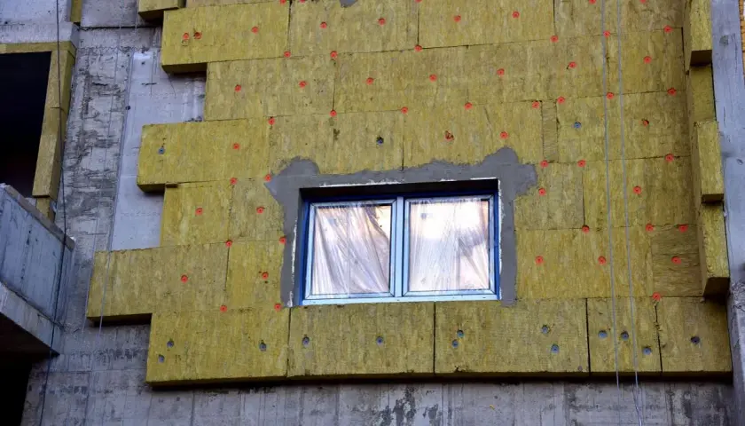 Pannelli isolanti gialli fissati con chiodi rossi mostrano come funziona il cappotto termico su un edificio in costruzione.