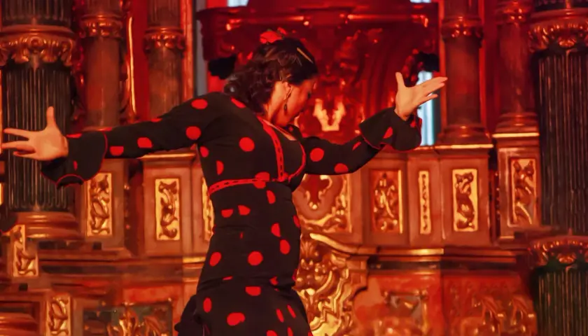 Tancerka flamenco w czarnej sukience w czerwone grochy, pełna **allegria**, porusza się na tle bogato zdobionej, złotej sceny.